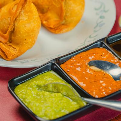 Samosa plate with various chutneys on the side.