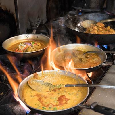 Three pans with simmering curry dishes on a gas stove with visible flames.
