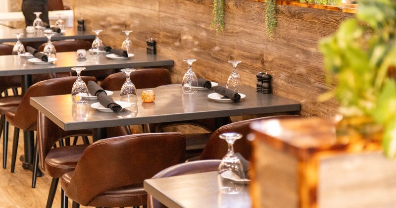 Interior, neatly set tables, brown leather chairs, wine glasses, plates, decorative candles