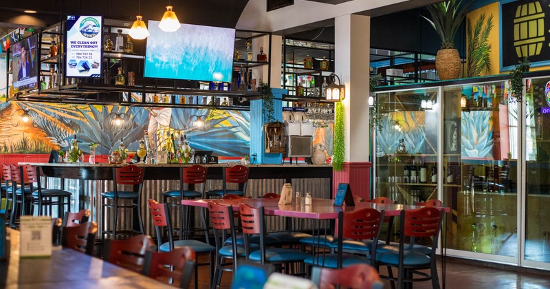 Interior of a lively bar with colorful murals, red chairs, and a glass partition