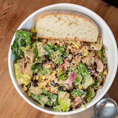 Rice bowl with lettuce, short rib, tomato, corn, roasted onion, beans, avocado, and sriracha.