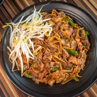 Stir-fried flat noodles with chicken, peppers, and bean sprouts on a black plate.