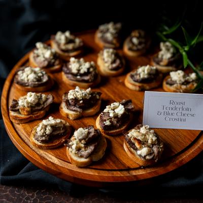 Crostini topped with roast beef and crumbled blue cheese on a wooden board.