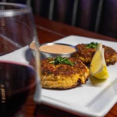Two Crab cakes in background with a glass of wine in the foreground.