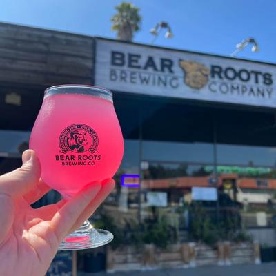 Person holding a glass of pink drink in the air, the company's building in the background.