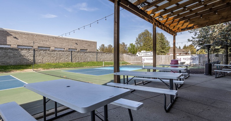 Exterior, partially covered seating area, plastic top picnic tables, tennis courts in the back