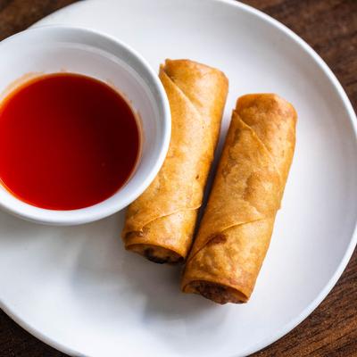 Fried eggrolls served with red dipping sauce on a white plate.