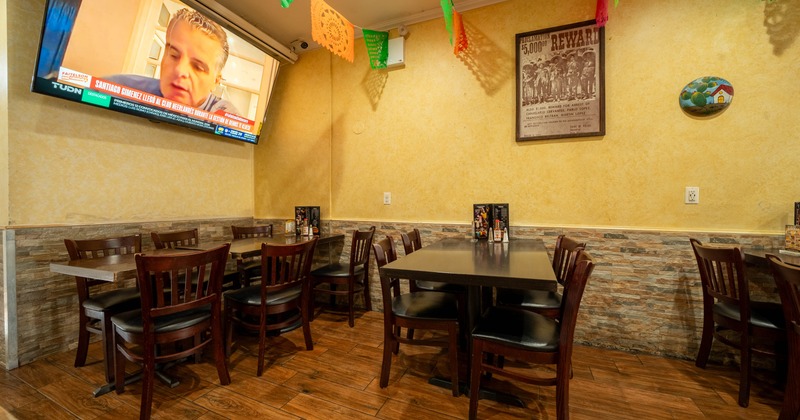 Restaurant interior with tables, chairs, colorful flags, a mounted TV