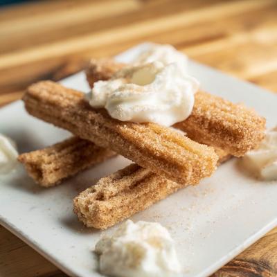 Churros dusted with cinnamon sugar and served with dollops of whipped cream.