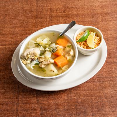Bowl of Mexican chicken soup served with a side of rice and lime wedges.