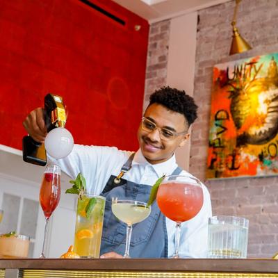 Bartender behind the bar with assorted cocktails in front.