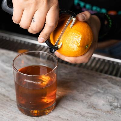 Bartender peels an orange for Old Fashioned cocktail