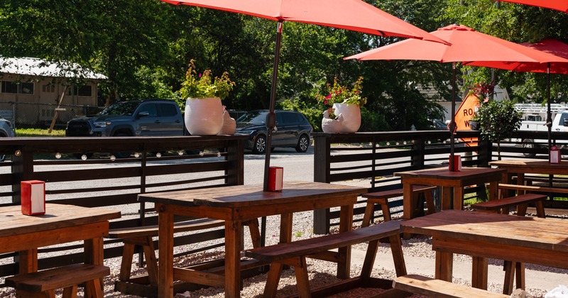 Outdoor seating area with wooden tables, red umbrellas, and plants