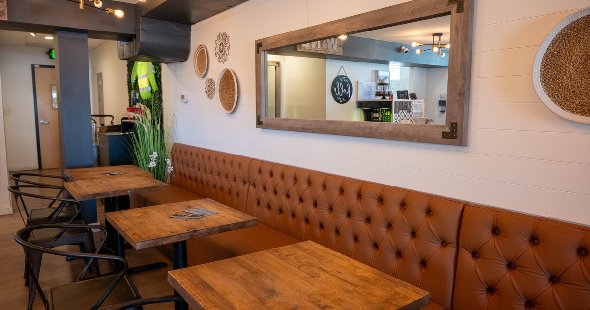 Modern cafe interior with tan tufted bench, wooden tables and decorative wall hangings