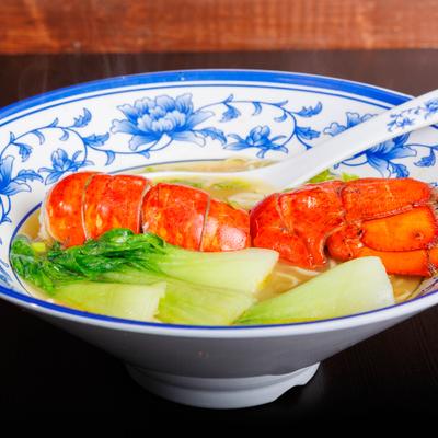 Lobster noodle soup with bok choy in a blue floral bowl.