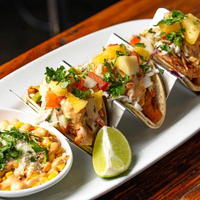 Three salmon tacos topped with pineapple, served with a side of street corn salad.