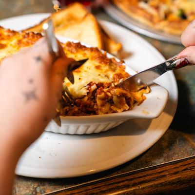 Person cutting baked pasta in a white dish on a table.