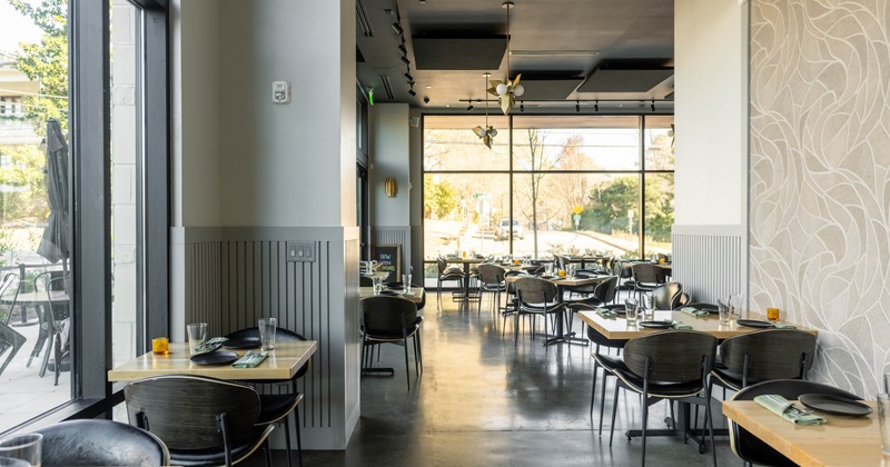 Interior of a modern restaurant, wooden tables, black chairs, large windows, and decorative walls