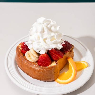 French Toast topped with strawberries, banana slices, and whipped cream on a white plate.