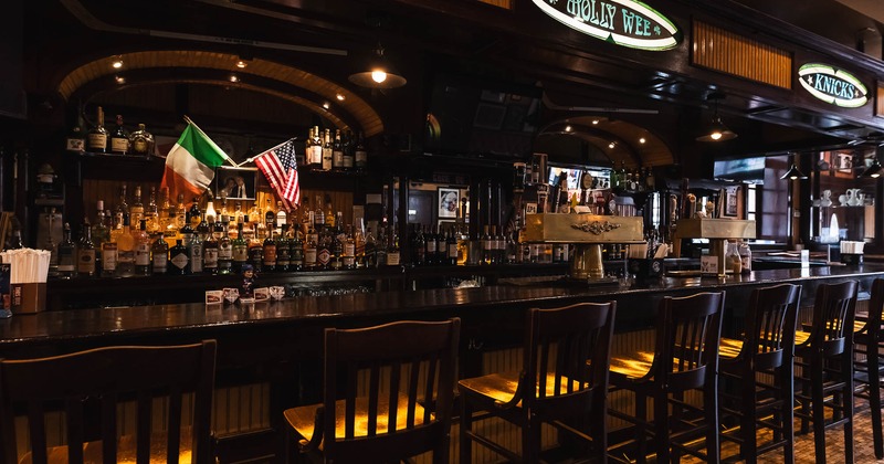Wooden bar interior with stools, Irish and American flags, and liquor on shelves