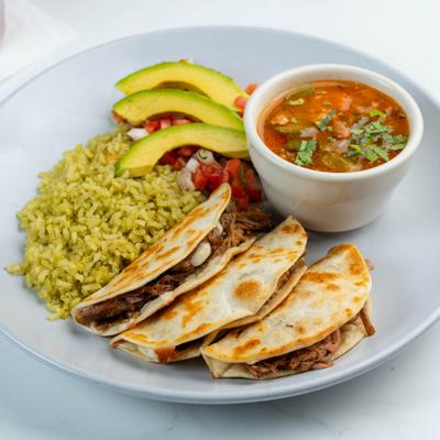 Birria taco plate with green rice, avocado slices, birria broth, and pico de gallo.