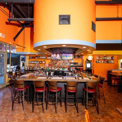 Modern interior with a prominent U-shaped bar, tables and chairs, and orange walls.