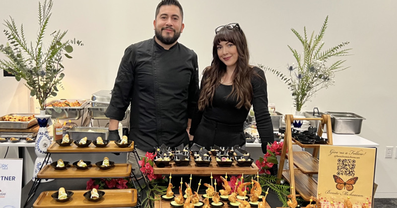 A chef and a staff member stand behind a lavish catering spread