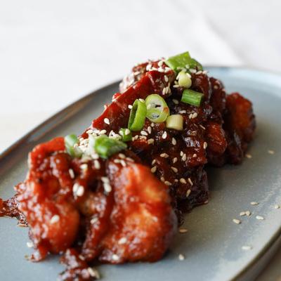 Crispy cauliflower dish covered in sauce, topped with sesame seeds and green  onions.