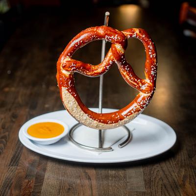 Salted soft pretzel on a metal stand, served with cheese sauce.