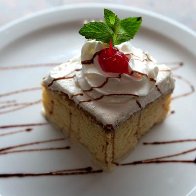 Tres leches cake topped with whipped cream, chocolate sauce and a cherry.