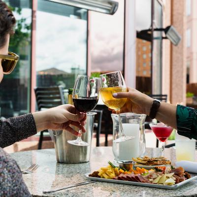 Two people toasting with wine over a table of food and drinks.