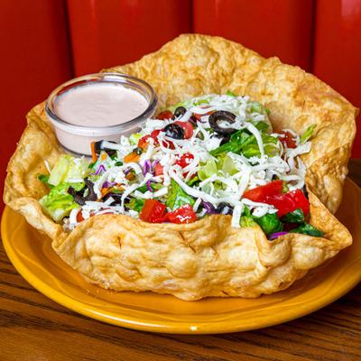 Taco salad in a tortilla bowl with dressing on the side.