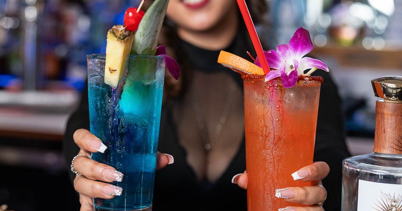A bartender holding two colorful cocktails