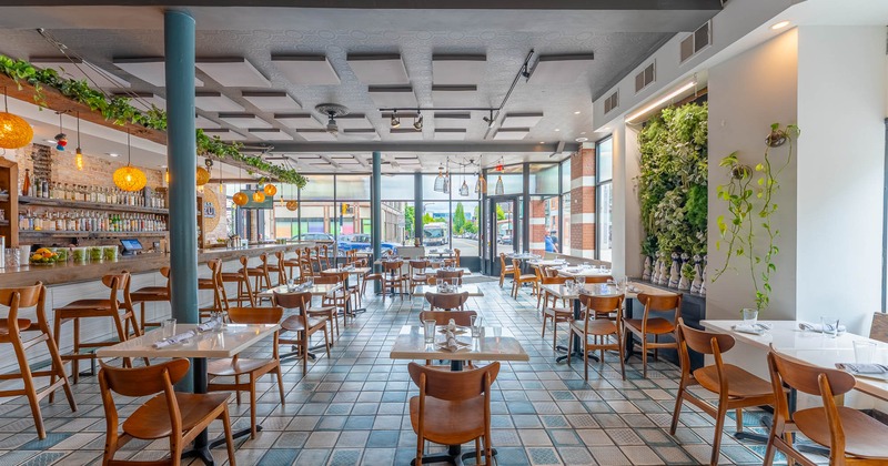 Interior, open space dining area, tables and chairs, bar with stools, restaurant entrance