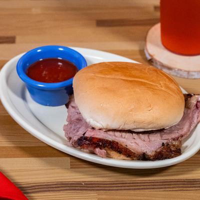 A plate holds a Brisket sandwich with a small cup of BBQ sauce.