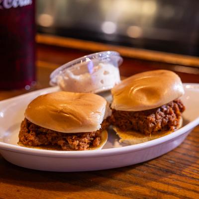 Two barbecue sliders served on a plate with a side of sauce.