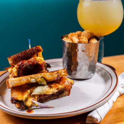 Grilled sandwich served with tater tots, accompanied with a margarita cocktail.