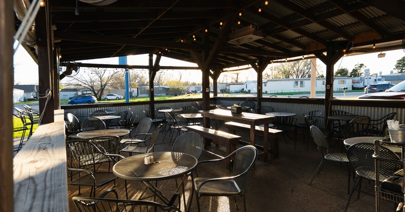 Outdoor seating area under a pavilion with metal tables and chairs, wooden picnic tables