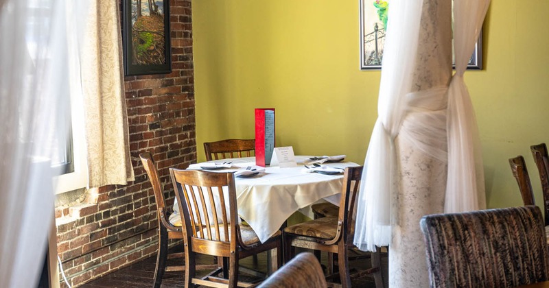Interior, table for four in the corner ready for guests, brick wall and window on the left