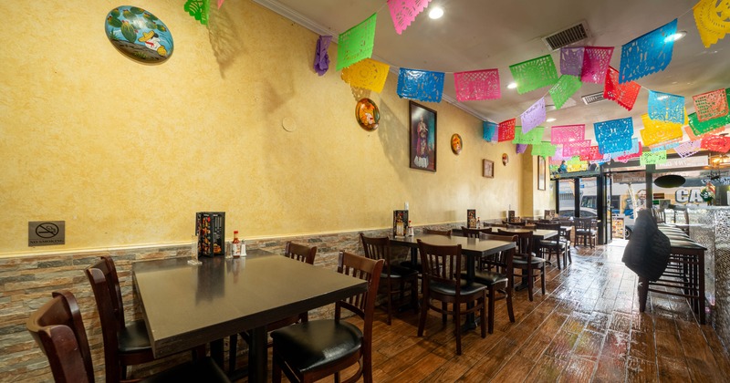 Interior of a restaurant with wooden tables, papel picado decorations, and yellow walls