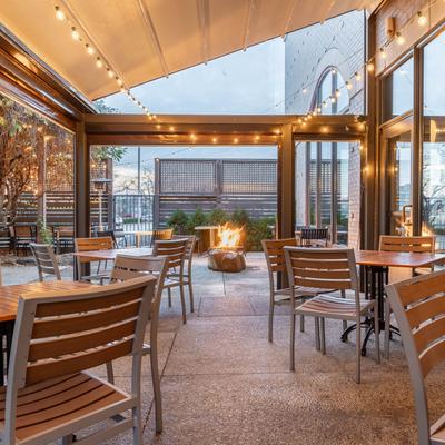 Outdoor patio with tables, chairs, string lights, and a central fire pit.