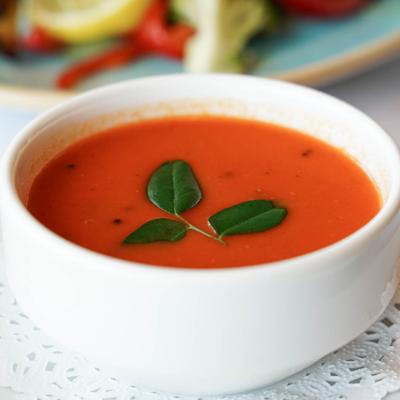 A bowl of a creamy tomato soup garnished with fresh leaves.