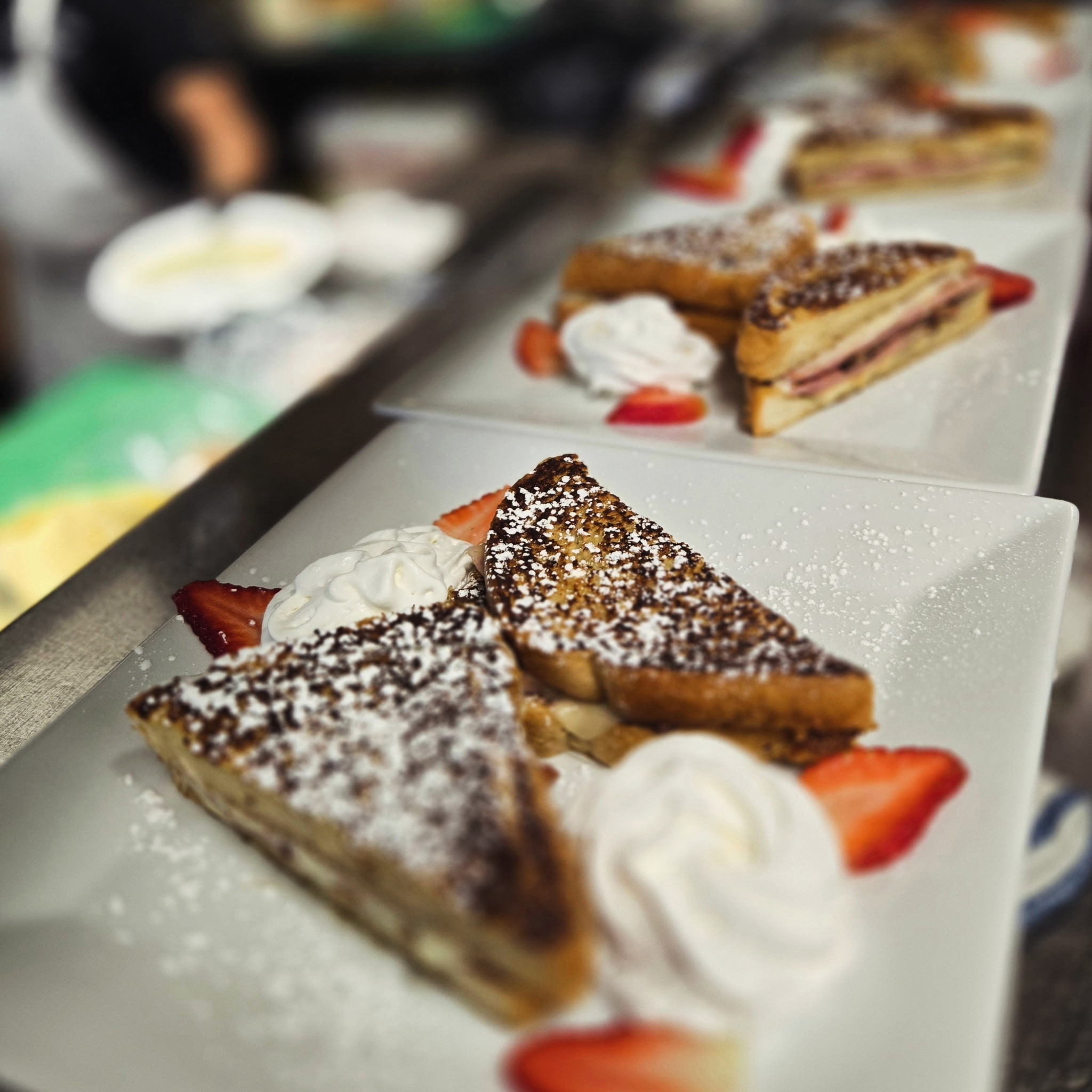 Several plates with French toast triangles topped with whipped cream and strawberries
