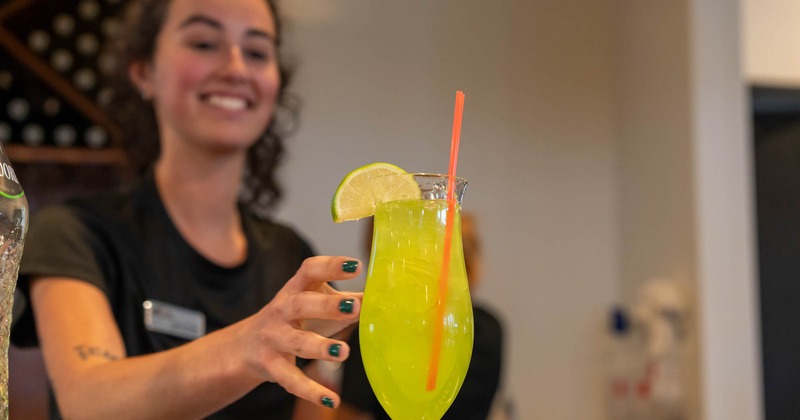 A bartender serves a cocktail drink on a bar counter