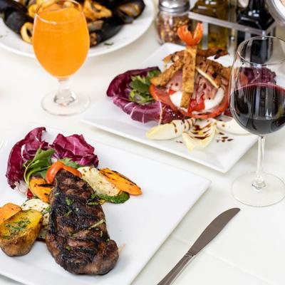 New York Strip Steak and Caprese Tower served with red wine and an orange drink.