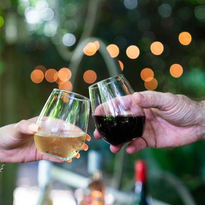 Two hands clinking glasses filled with white and red wine.