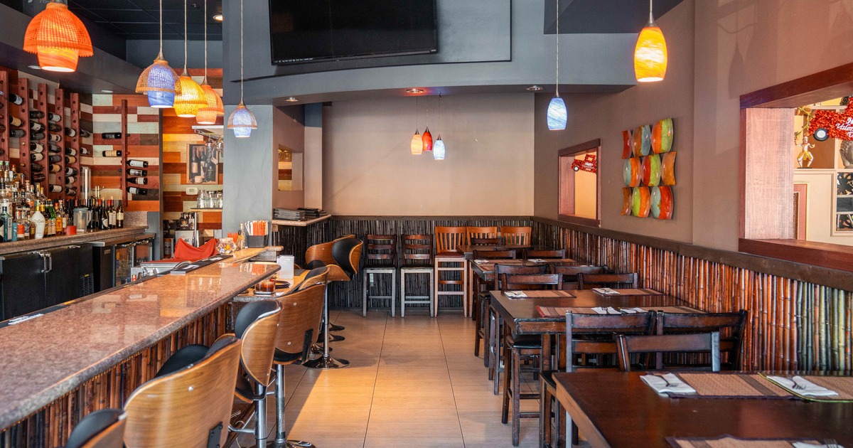 Interior of a modern restaurant showing a bar, colorful pendant lights, and dining tables