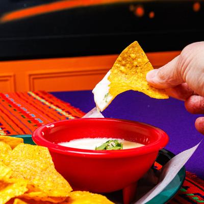 Hand dipping tortilla chips into a bowl with queso dip.