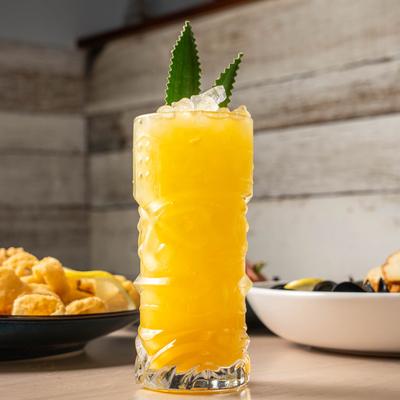 The Hidden Oasis cocktail, a refreshing yellow drink garnished with pineapple leaves.