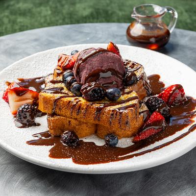 French toast topped with berries and chocolate sauce, alongside a syrup.